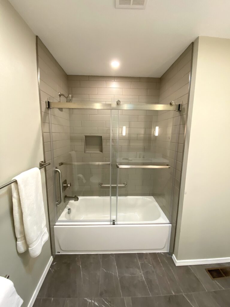 Remodeled bathroom with tiled tub-shower, sliding glass door, recessed niche, and grab bars