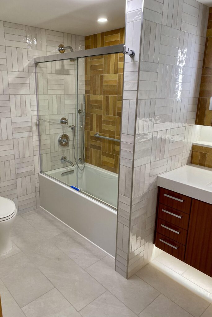 Remodeled bathroom with white patterned tile tub-shower, wood-tone accent tile, and floating wood vanity