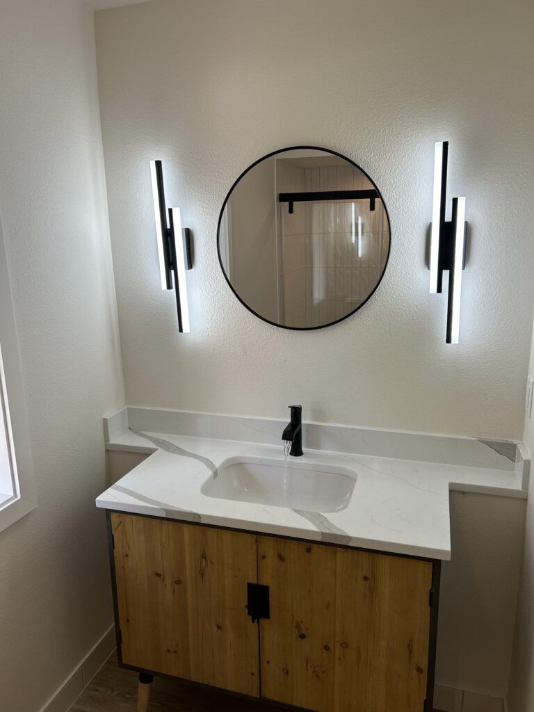 Bathroom vanity with wood cabinet, quartz top, matte black faucet, round mirror, and LED wall sconces