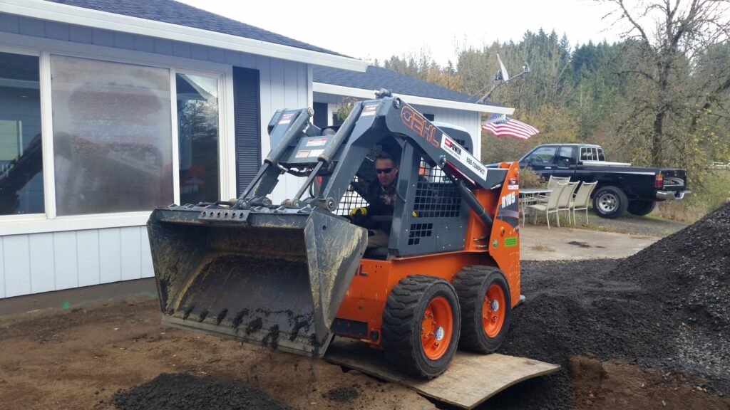 Brandan Keyser operating an orange Gehl skid steer, moving gravel beside a house
