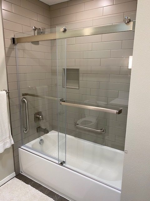 Remodeled bathroom with tiled tub-shower, frameless sliding glass doors, recessed niche, and grab bars