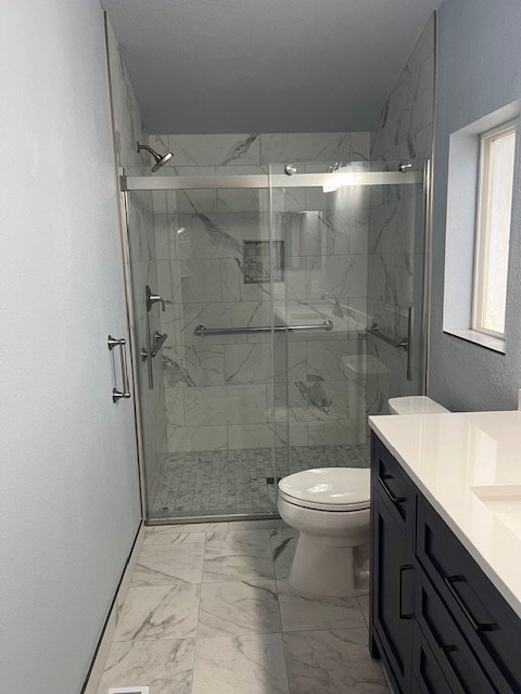 After: walk-in shower with marble-look tile, glass sliding doors, grab bar and recessed niche