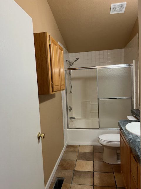 Before: dated bathroom with fiberglass tub-shower combo, framed sliding glass doors and brown floor tile