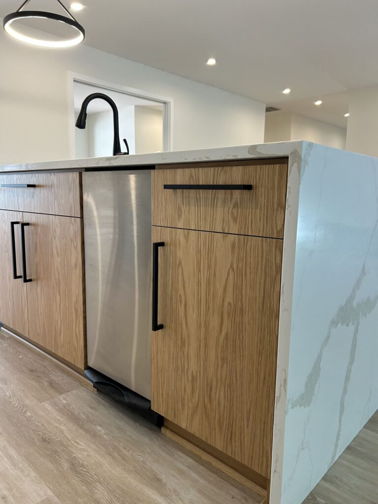 Kitchen island with wood slab-front cabinets, black bar pulls, built-in dishwasher, and marble-look waterfall countertop