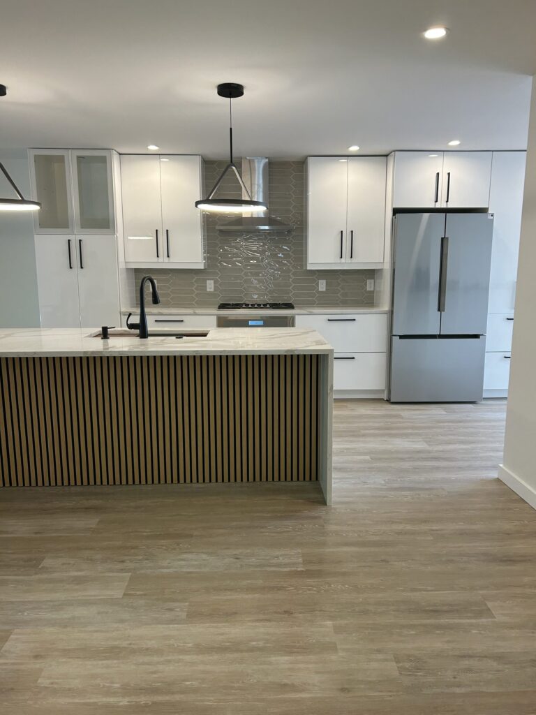 Remodeled kitchen with white flat-panel cabinets, slatted wood island with waterfall countertop, and black pendant lights