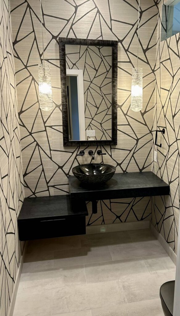 Powder room with geometric wallpaper, floating black vanity, vessel sink, wall-mount faucet, and glass pendant lights